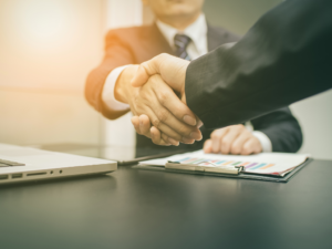 Close-up cropped photo of two businessmen in suits shaking hands, successful business acquisition made possible by business investment loans