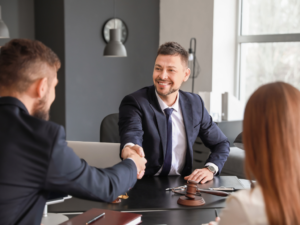 A man seated next to a woman shakes hands with another man seated across them, a business owner and a lender agreeing on a second mortgage loan