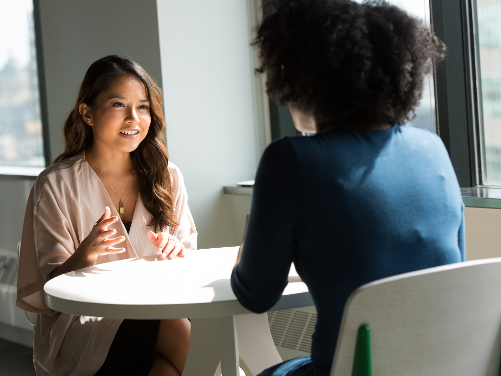 Two women seated across each other and talking in a professional setting, a borrower and a lender or broker discussing a second mortgage loan