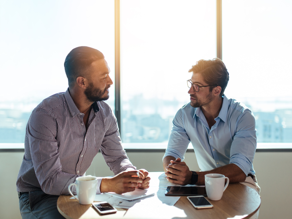 Two men seated across each other discussing business matters, a business owner and a lender or broker discussing loan terms