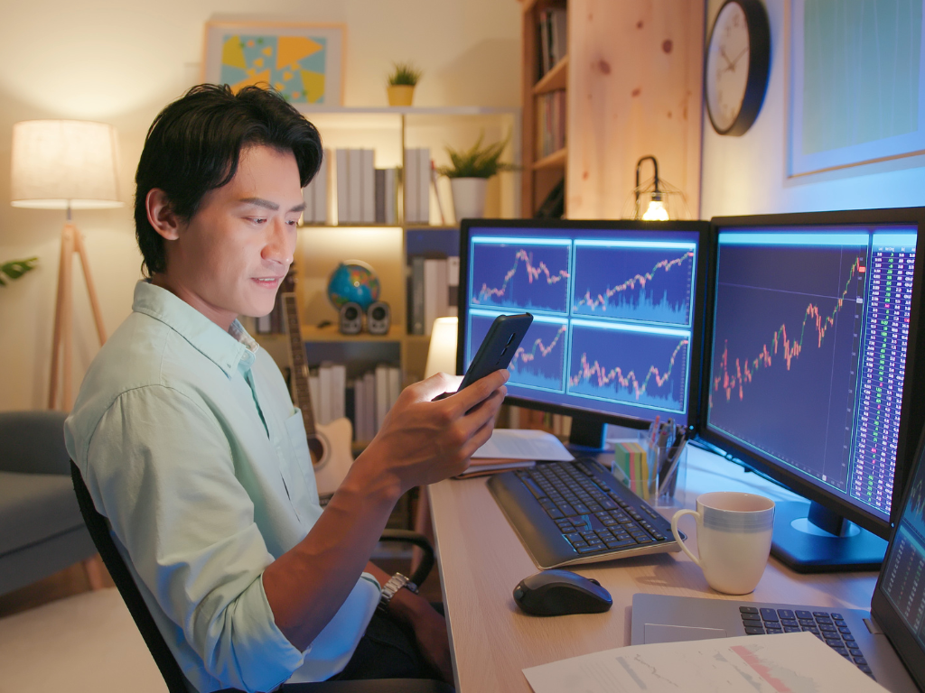 A man seated in front of multiple monitors showing the stock market, investing in stocks as part of a debt recycling strategy