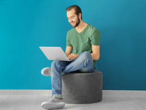 A smiling man seated half cross-legged on a grey chair while using his laptop, learning how to debt recycle in Australia