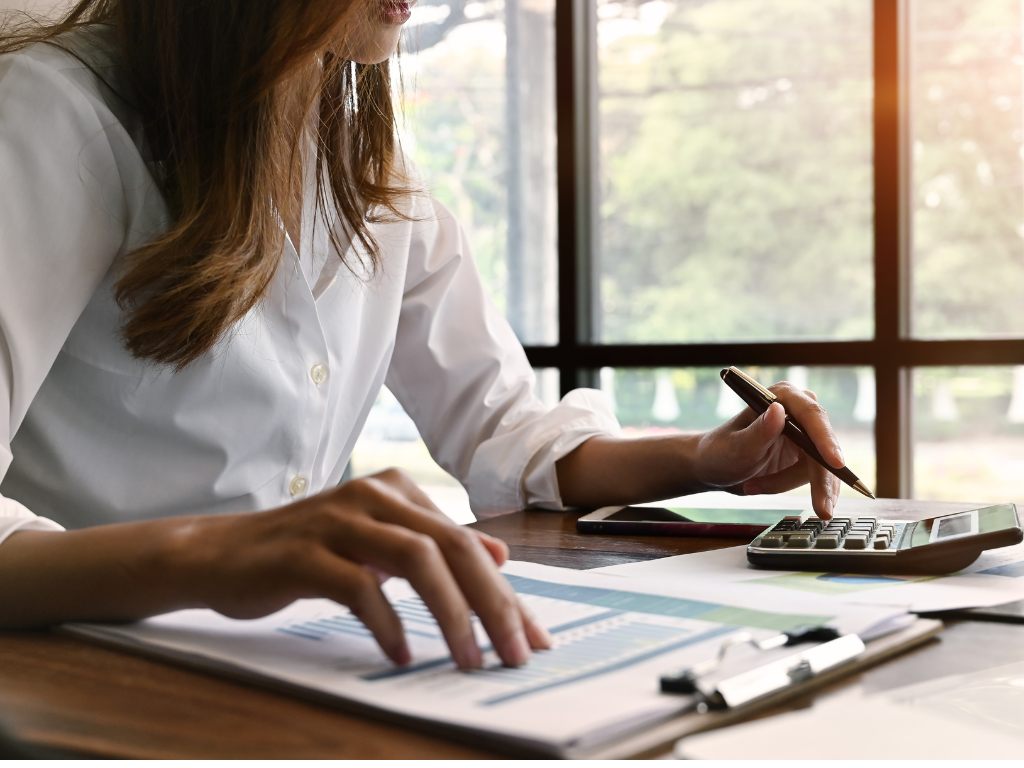 Cropped photo of a woman using a calculator and going over documents, calculating interest on a business loan to claim tax deductions