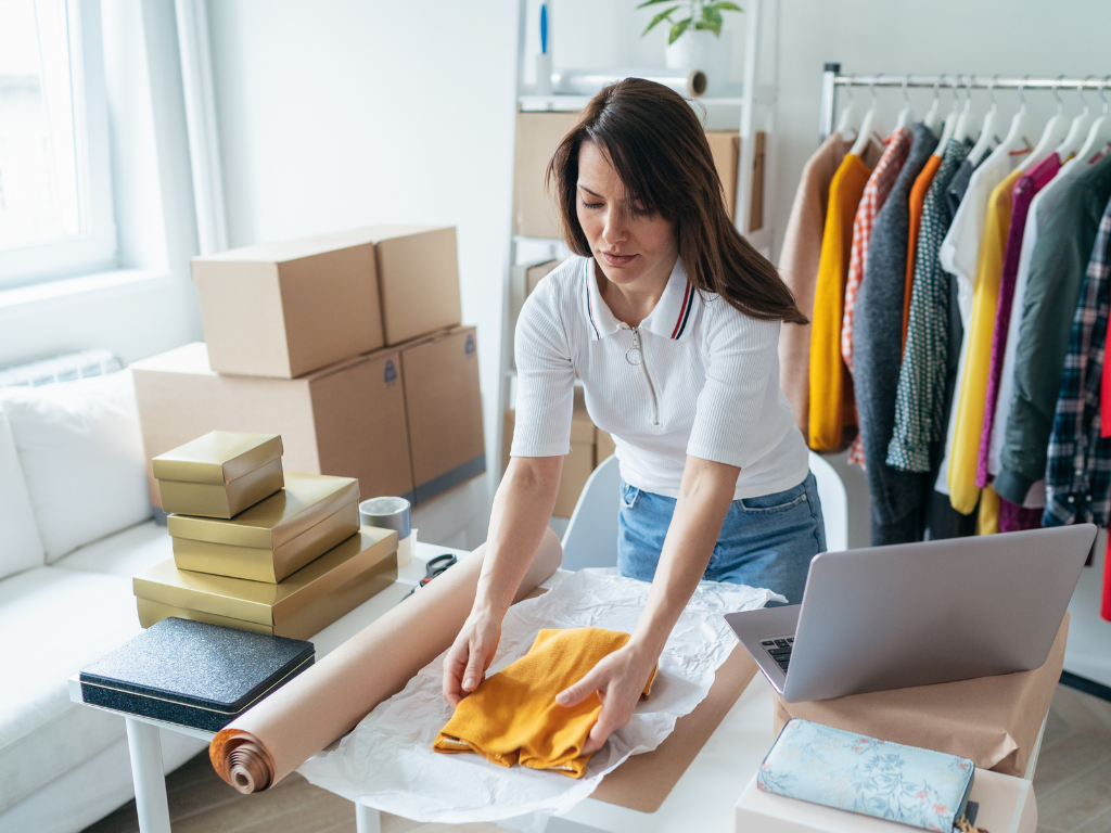 Woman wrapping a piece of clothing, business owner packing orders ahead of her business’s seasonal peak