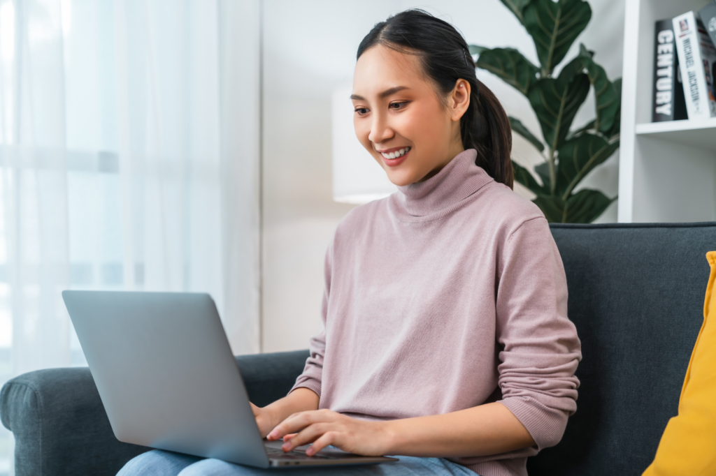 A woman smiles as she uses her laptop, non-resident startup business owner looking for financing options in Australia