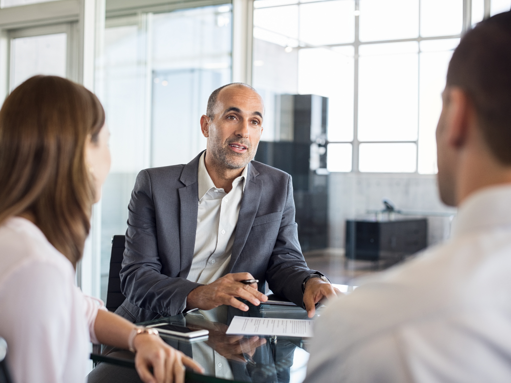 A man discusses business line of credit loans to borrowers, a man and a woman seated across him