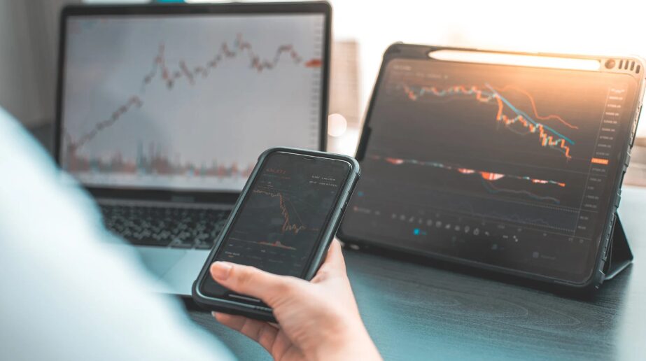 A businessman using a tablet and smartphone to analyse investment trends and stock market performance, highlighting the impact of rising bond yields, speculative markets, and the fragility of the U.S. economy on global and Australian markets.