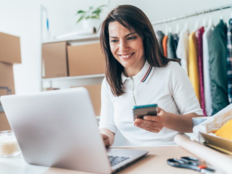 A business owner making a transacation on her laptop as she holds her smartphone