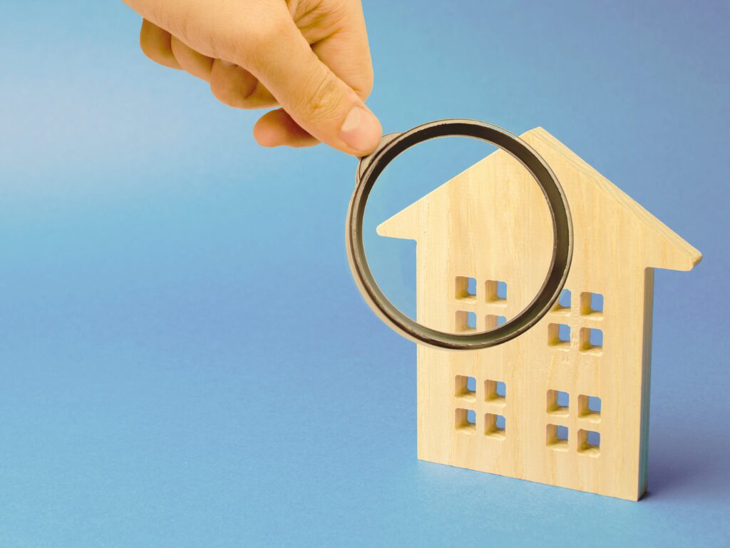 A hand holding a magnifying glass examining a wooden miniature model house, concept photo for a bank valuation of a property