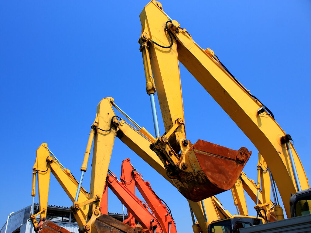 Cropped photo of the arms of three industrial diggers, with their yellow paint contrasting against a bright blue sky, equipment purchased with no-doc equipment finance