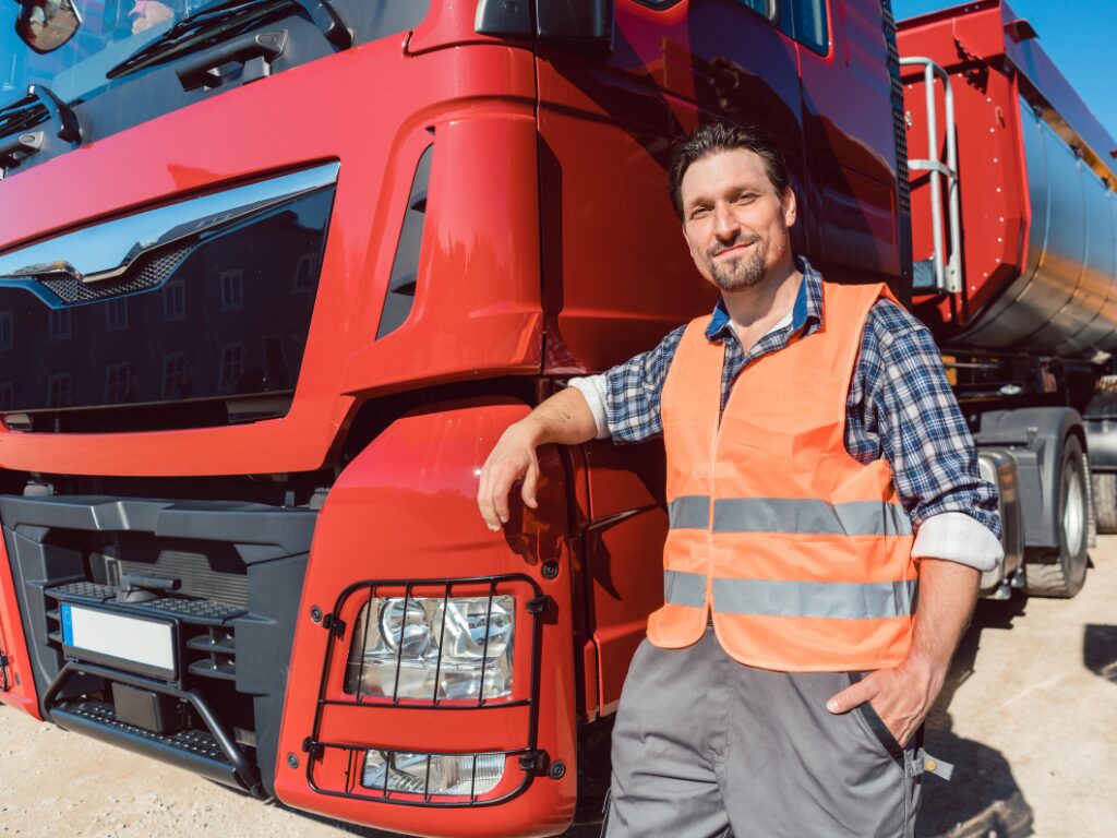 A man in a high-visibility jacket poses, leaning against the front of a large red truck, concept photo of a business owner and the truck he purchased with no-doc equipment finance