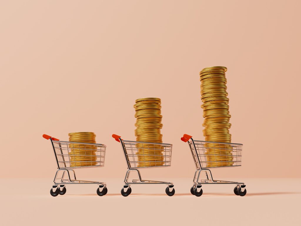 Three miniature model shopping carts lined up carrying piles of coins in increasing order, concept photo of lifestyle creep, consumption rising together with income