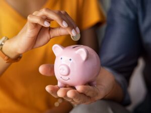 Cropped and zoomed photo of a man holding a piggy bank and a woman inserting a coin into its slot, concept photo of budgeting and saving to avoid lifestyle creep