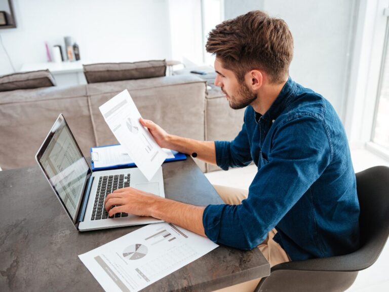 A man intently reads documents and types on his laptop, a man budgeting and managing finances to avoid lifestyle creep