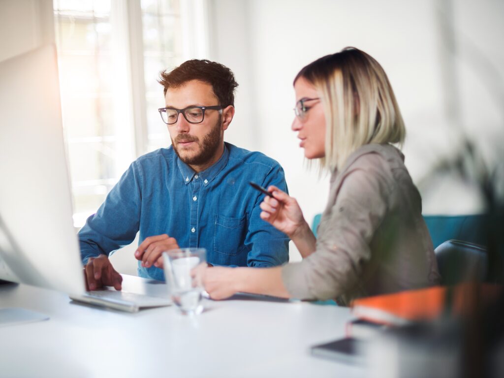 A man and a woman in a professional setting discuss business while using or looking at a computer screen, business owners discussing working capital loans