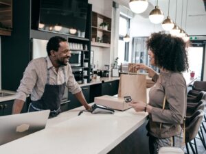 A man attending to the cash register smiles as a shopper pays for and receives her goods at a retail store