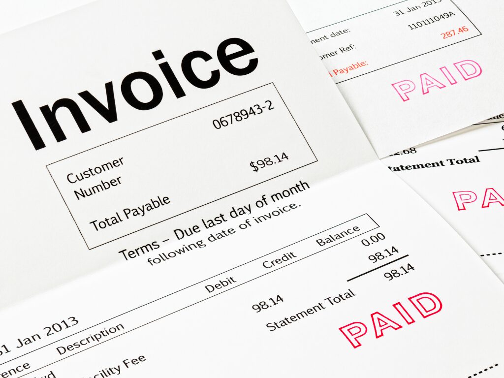 Zoomed in and cropped photo of many invoices with the word paid stamped on each in red ink, invoices paid which means the invoice financing arrangement will be paid