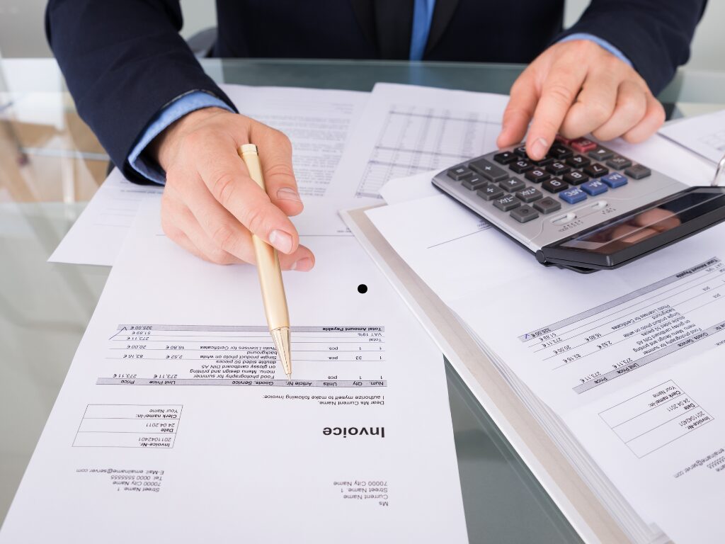 Cropped photo of a man calculating the value of his customers’ unpaid invoices, man using calculator while looking at an invoice