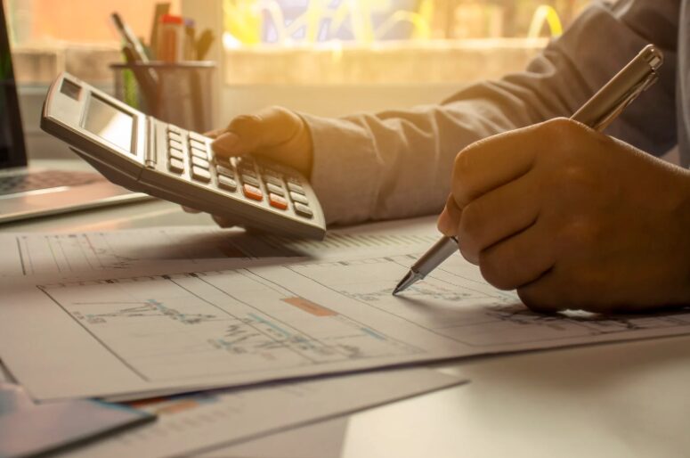 Hands holding a pen and calculator over documents, carefully weighing the benefits and drawbacks before completing all fitout finance qualifications.