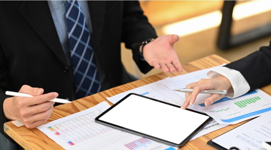 Two professionals with pens in hand reviewing bank vs non-bank lenders for working capital financing on a blank tablet screen, discussing working capital loan options and flexible funding solutions.