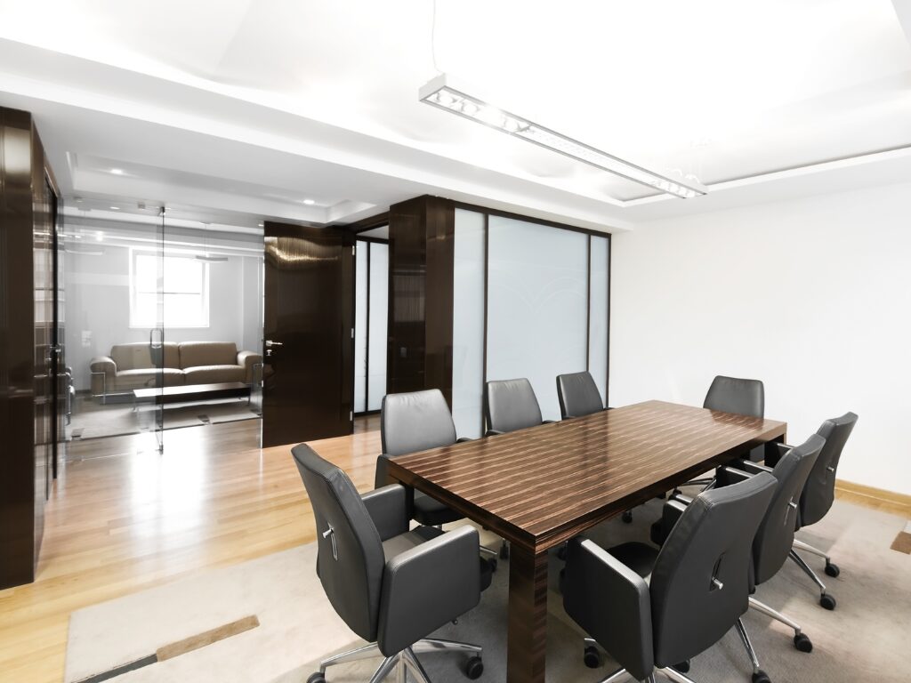 An empty office conference room with a long dark wood table and several black office chairs, office fitout design