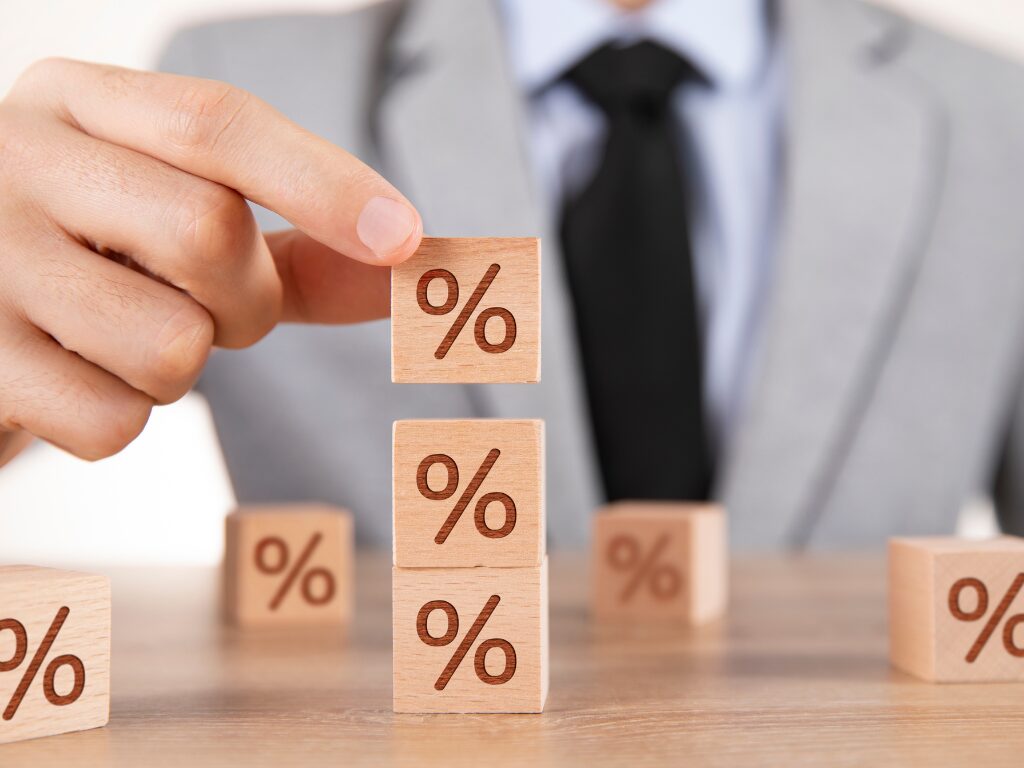 Cropped photo of a man in a grey suit stacking together small wooden blocks with a percent sign printed on them, concept photo for interest only loans or paying only interest on a loan