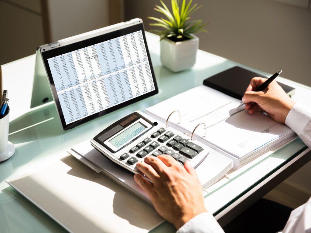 Cropped photo of a man looking at invoices on his computer tablet while calculating finances using a calculator a large paper binder, business owner considering accounts receivable financing