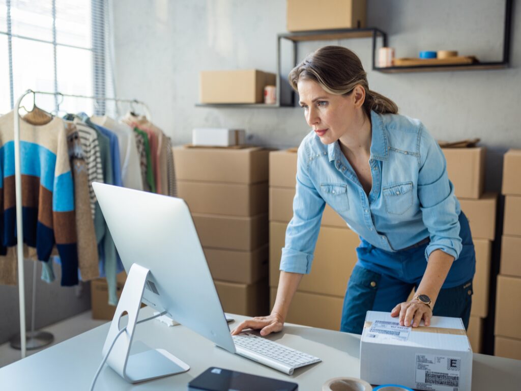 A woman crouches over her computer and looks at the monitor intently while holding a package box, business owner in need of immediate funding and looking at AR financing options