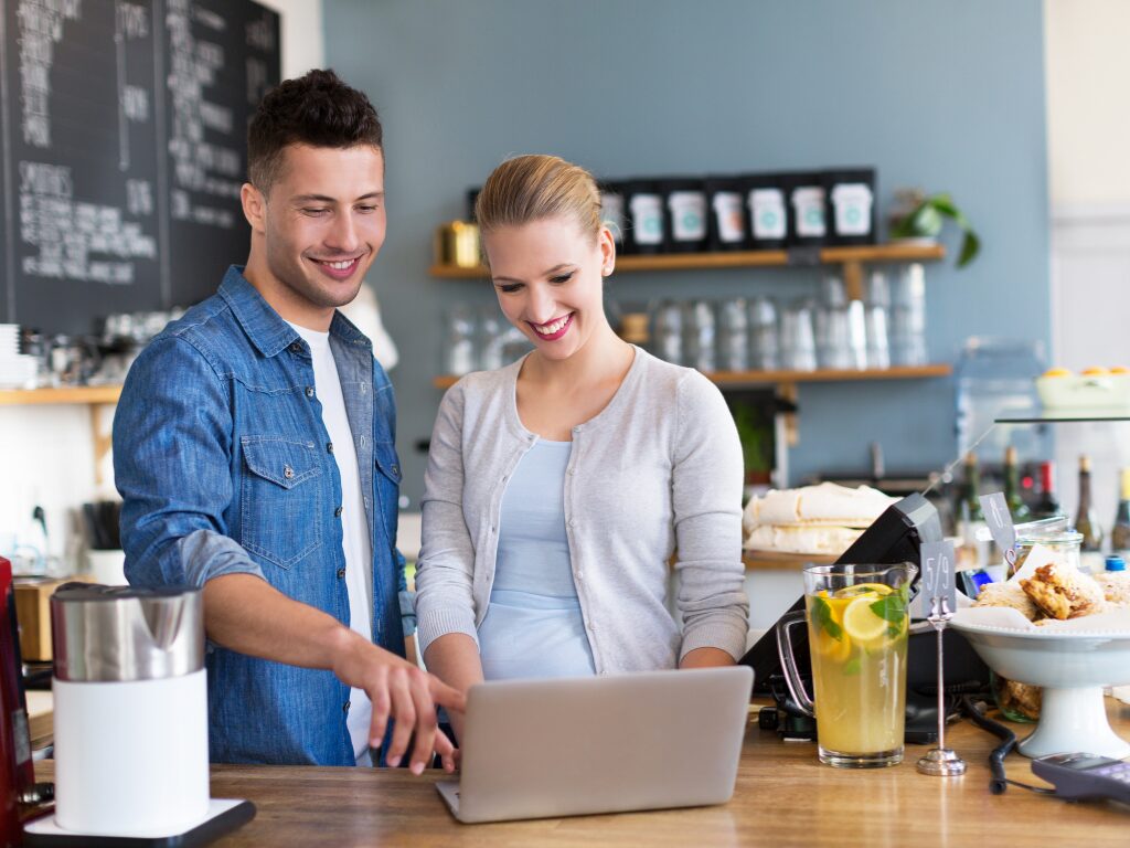 Two business owners cheerfully discuss while pointing at the display of a laptop, Cafe owners discussing working capital solutions for small business