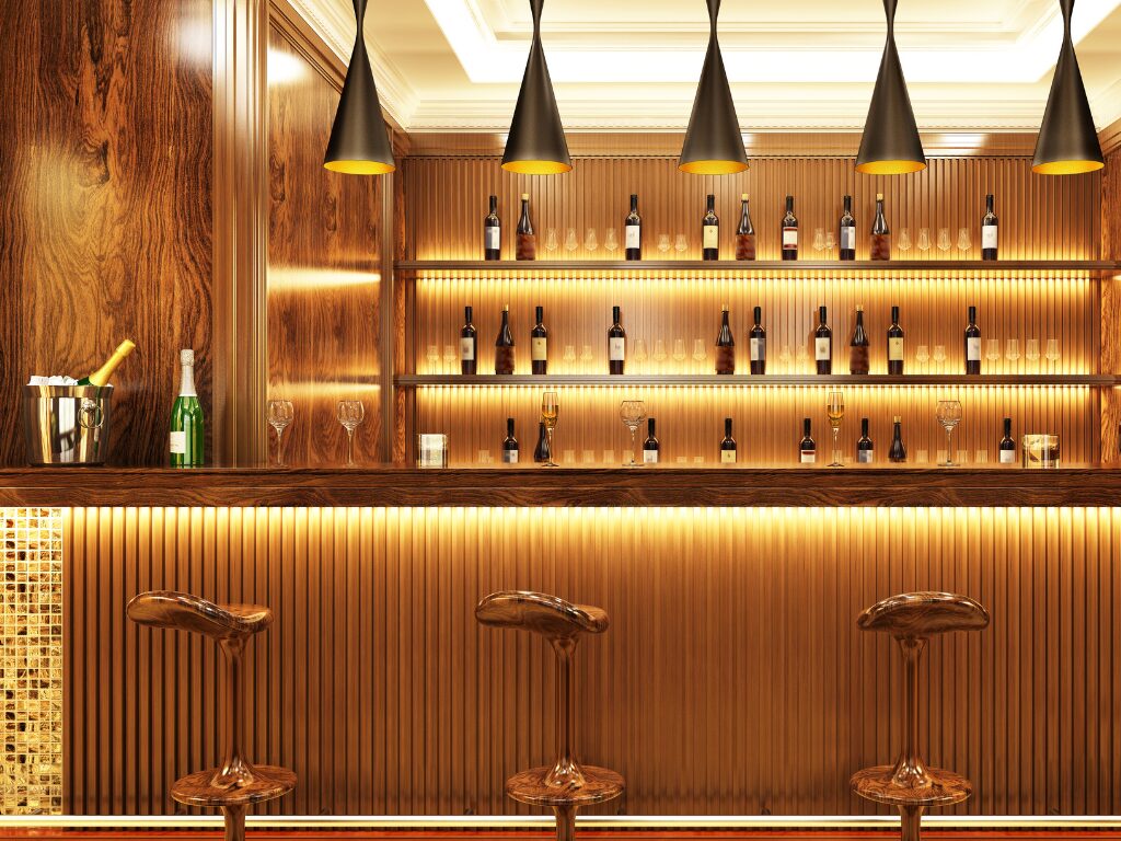 Elegant and luxurious bar with wood panelling, warm lighting, and mosaic tiling, bottles of liquor are displayed at the back while three metallic bar chairs are placed in front