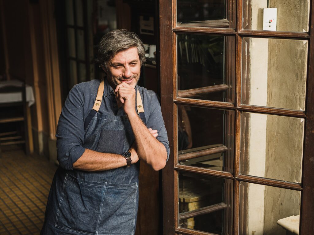 A business owner leans against the front door of his business space smiling with his hand on his chin, business owner with positive working capital due to working capital funding