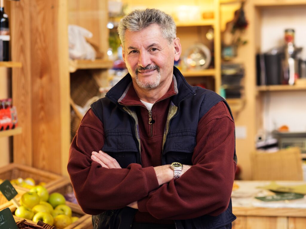 A man inside a retail store poses arms crossed and smiles directly at the camera, business owner inside his premises is happy because he secured a working capital loan