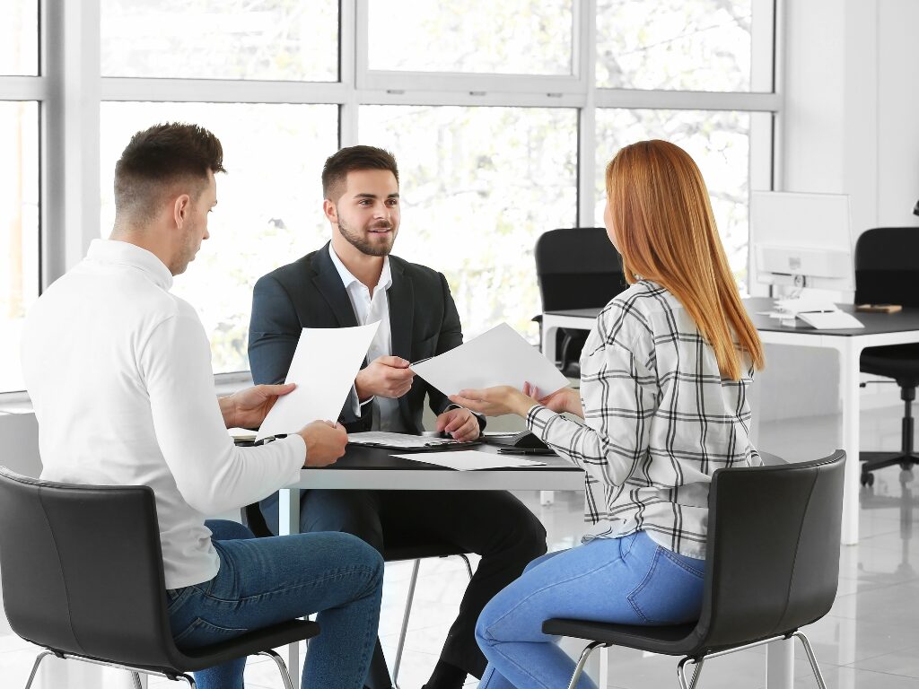 A man and a woman holding documents sit across a man in a suit, business owners discussing eligibility requirements for a working capital loan with a loan expert or lender