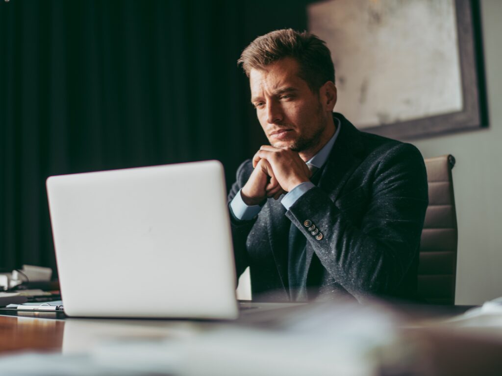 A man in a suit reads the display of his laptop with a serious expression, a business owner dealing with working capital funding application challenges