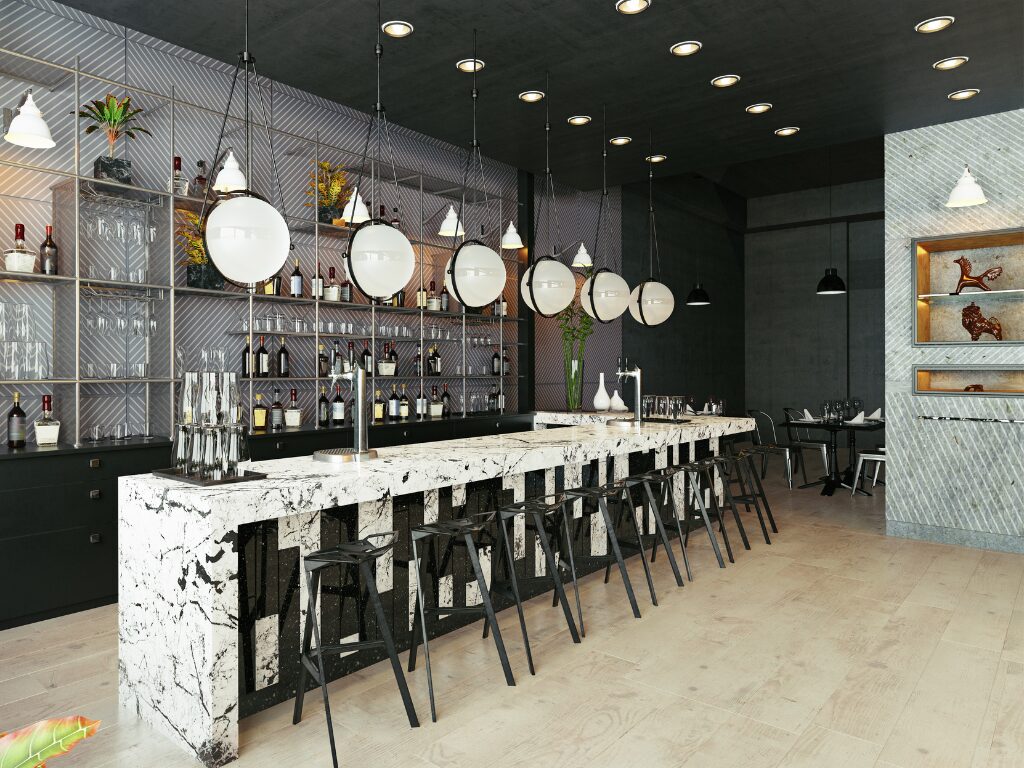 Modern designed bar with statement lighting, marbled bar top, sleek black chairs, stainless steel sleek shelving behind the bar