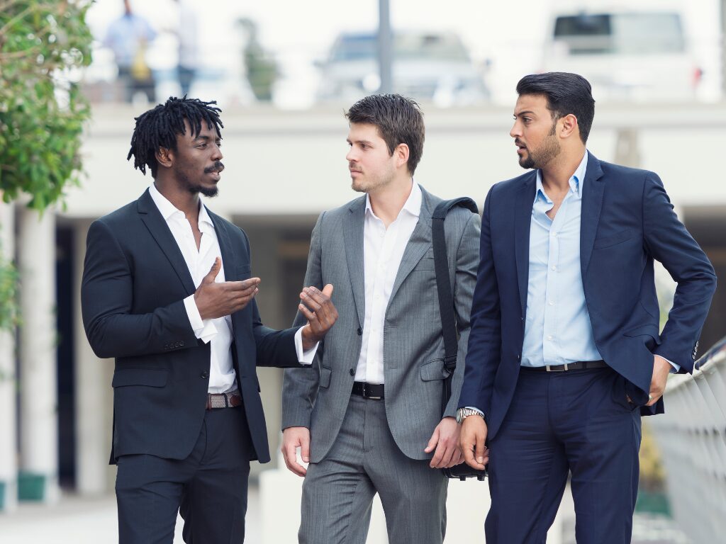 Three men in suits engaged in a discussion as they walk down a street in daylight, expats discussing solutions to tax debt with the ATO