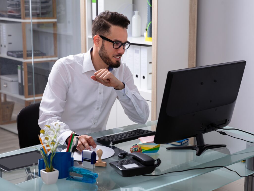 A man in a professional setting lightly smiles as he uses his desktop computer, expat finding tax debt solutions for his business in Australia