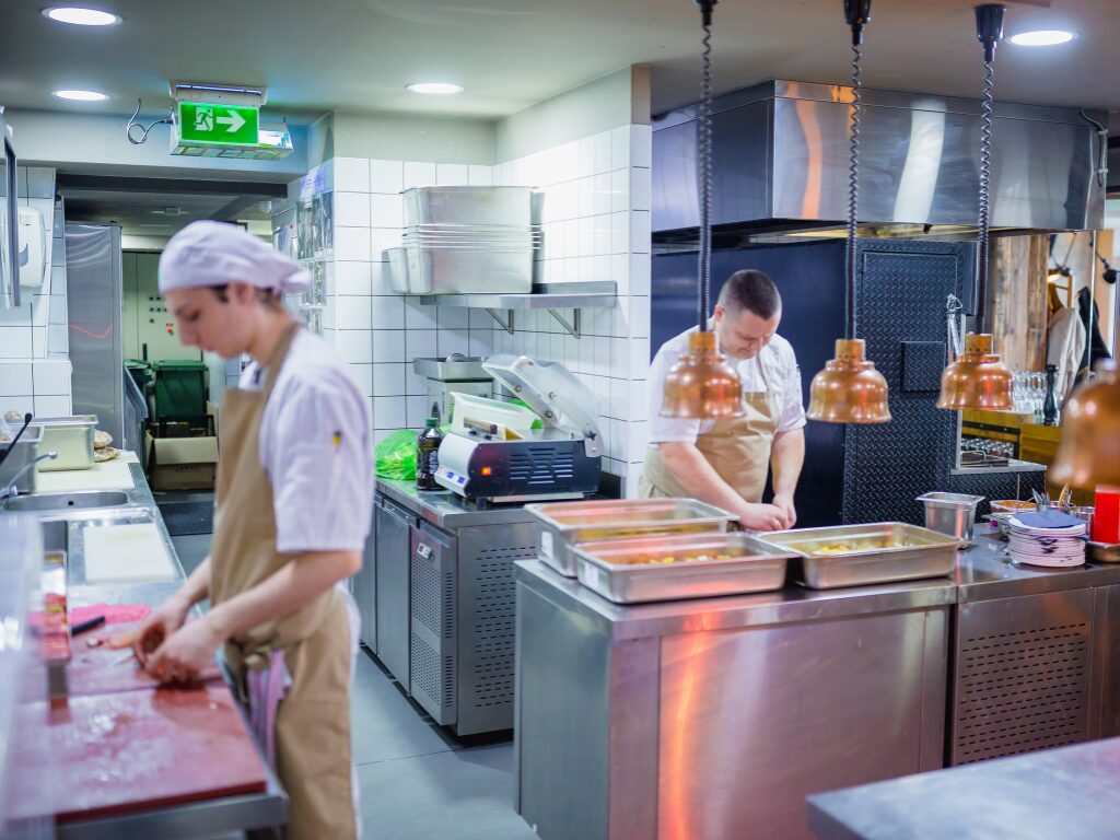 Restaurant workers inside a commercial kitchen doing prep for the day, fully equipped industrial kitchen