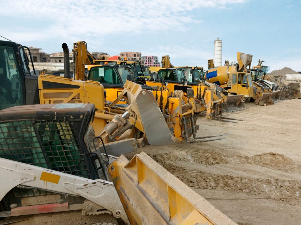 A row of various yellow large equipment for construction, digger, tractor, cement mixer, and other heavy machinery funded by bad credit equipment finance