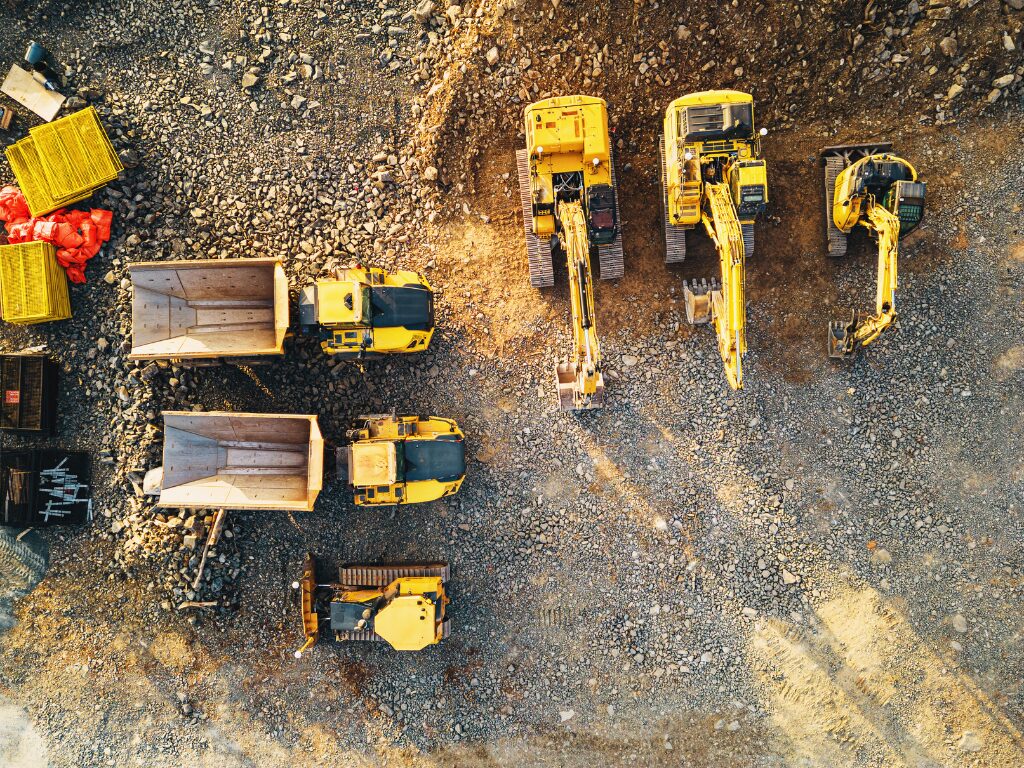 Bird’s eye view of several yellow heavy equipment for digging and construction, large wheeled machinery surrounded by gravel, rocks, and soil