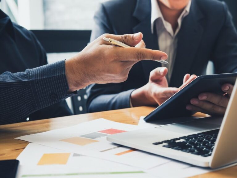 Two men in a professional setting discussing something on the display of an electronic tablet, strategising finances, planning debt recycling with interest-only loans