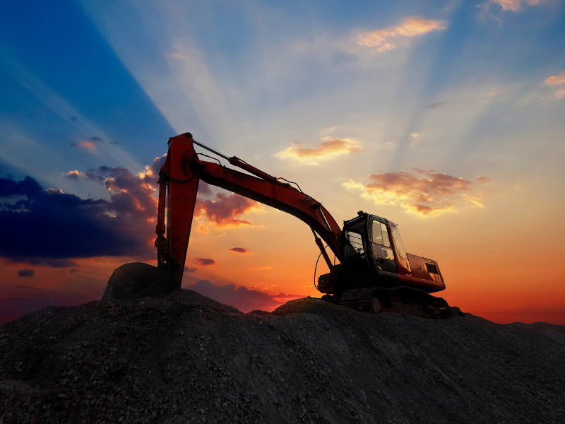 Large orange excavator set against a majestic sunrise