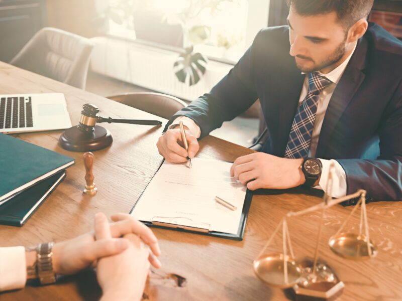 A man in a suit signs a legal document with a fountain pen, law scales and a judge’s gavel visible on the table, concept photo for signing legal documents or complying with Australian tax laws