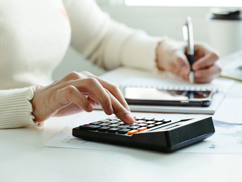 Cropped photo of a woman using a calculator and writing down results, calculating the cost of a tax debt loan