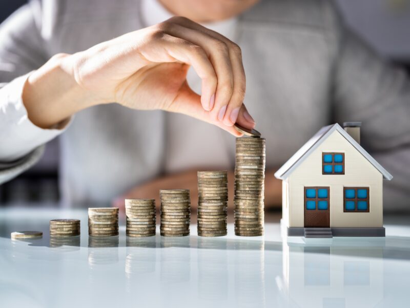 Cropped photo of a man stacking coins in increasing order next to a model miniature house, concept photo for an investor taking on loans to purchase investment property and build wealth