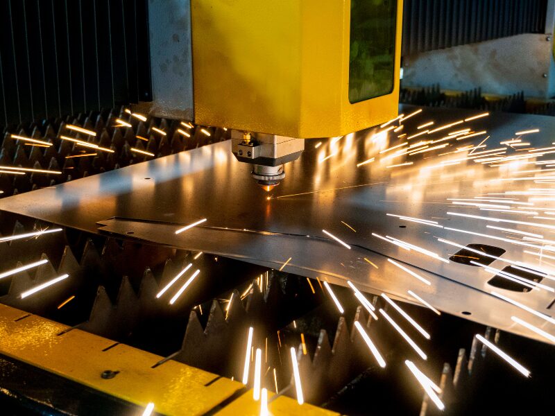 Industrial laser cutter, cutting a sheet of steel, sparks flying, machine funded by manufacturing equipment financing