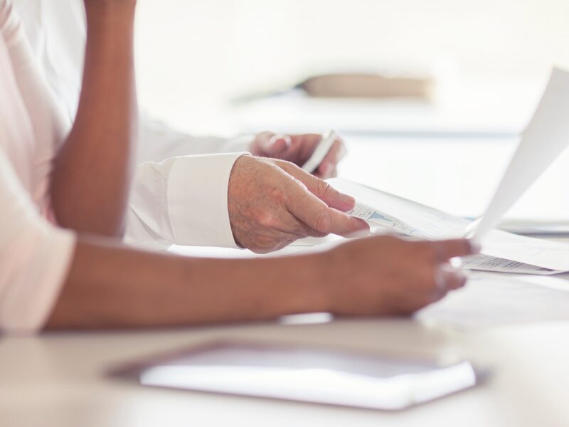 Cropped photo of two people discussing documents, showing only their hands