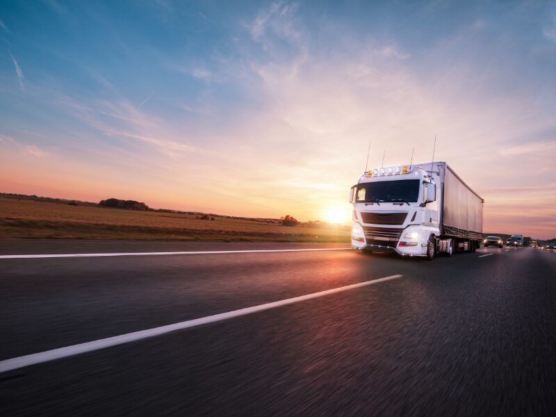 A white transport truck driving down a highway during sunrise
