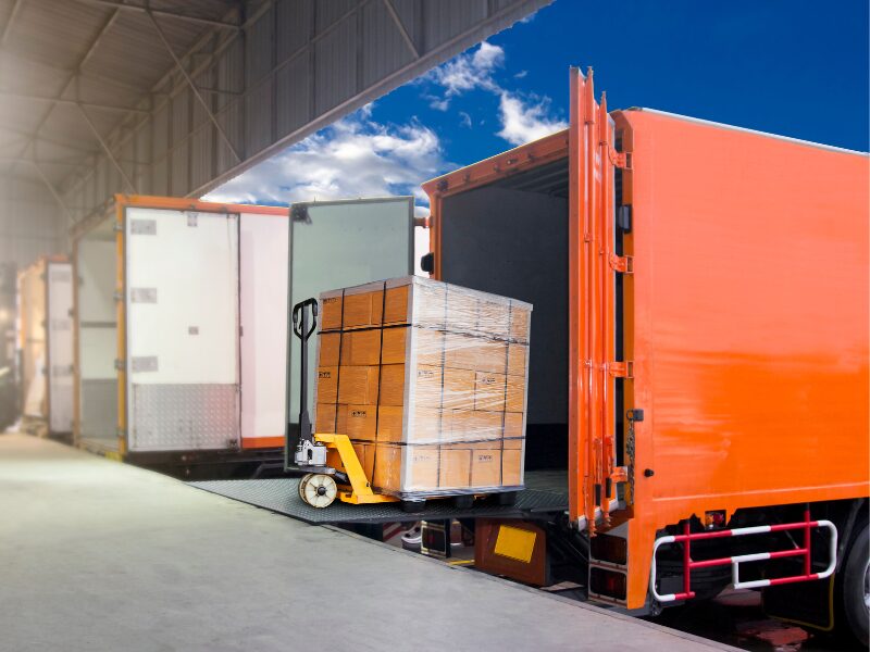 A pile of boxes being loaded onto a bright orange transport truck, logistics and trucking business