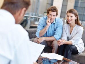 A couple sit across a lending expert or a lender discussing a refinancing loan to repay a caveat loan